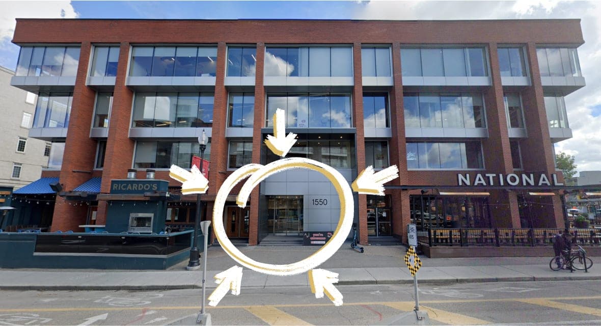 The front of 1550 5 St SW in Calgary, a red brick building with tall windows. The glass entrance doors under the grey panel marked 1550 are circled.