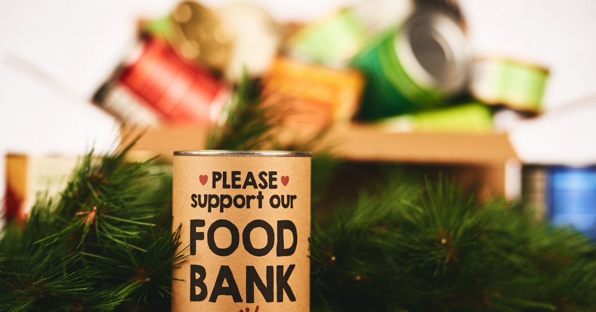 A tin labelled Please support our food bank in front of a box of canned goods, with evergreen branches around it