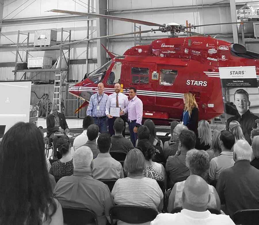 Jarrett Chisholm receiving his Critical Care Paramedic certification in the STARS hangar in Calgary, with the air ambulance behind him